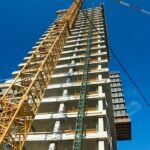 Low-angle view of skyscraper under construction with crane, clear blue sky.