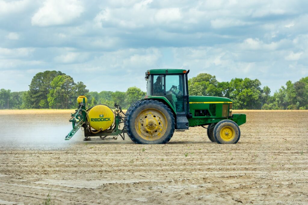 Green tractor with sprayer working in an open farm field under a cloudy sky.