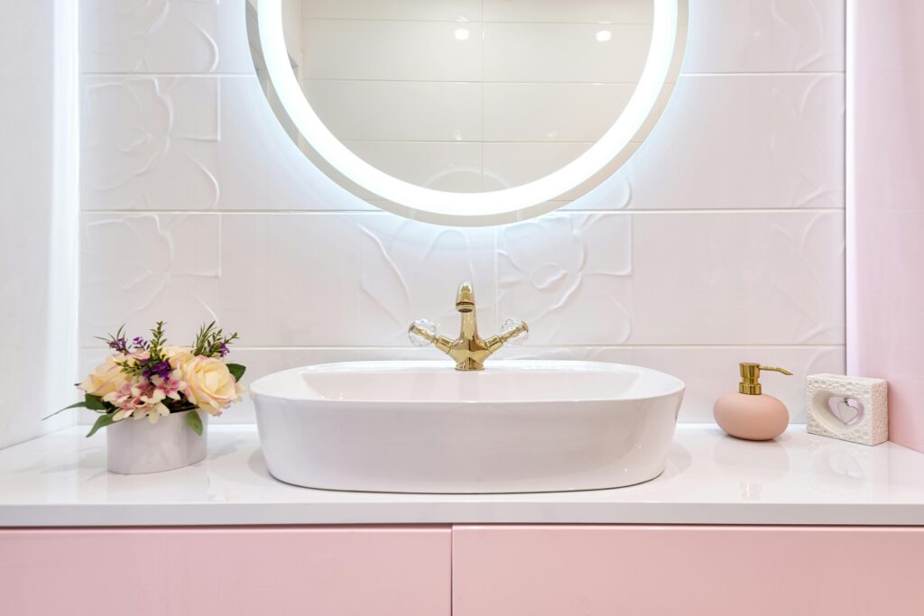 Interior of modern bathroom with luminous mirror hanging under sink with faucet near blooming flowers and soap